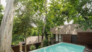 A swimming pool surrounded by trees and a wooden deck. - Rumah Lituhayu (Tabanan)