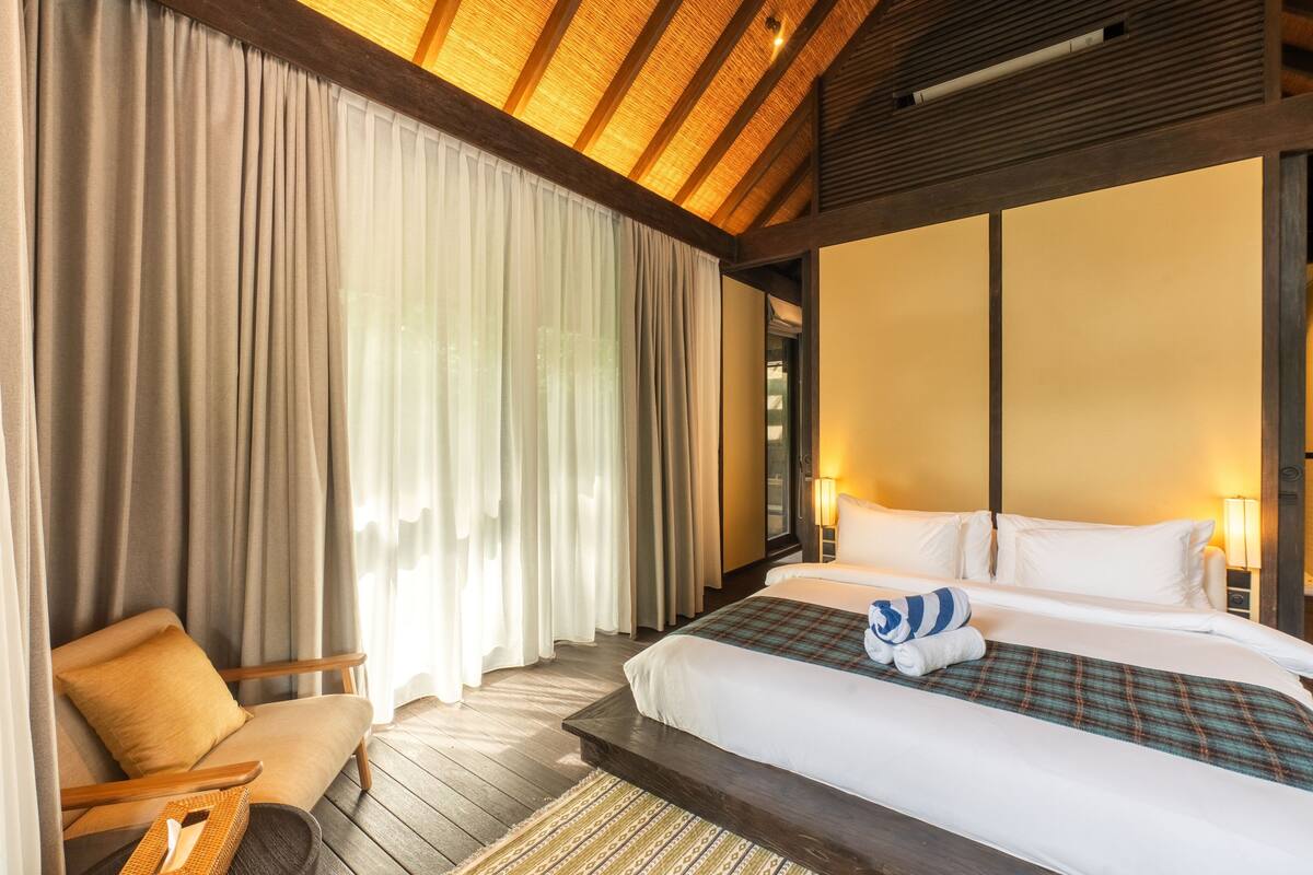 Una habitación de hotel con una cama grande, una silla y techo de madera.