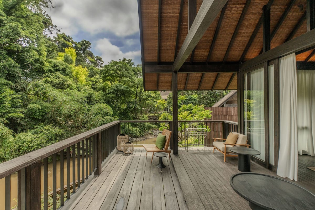 Una terraza de madera con mobiliario exterior, un pérgola y vistas a abundante vegetación.