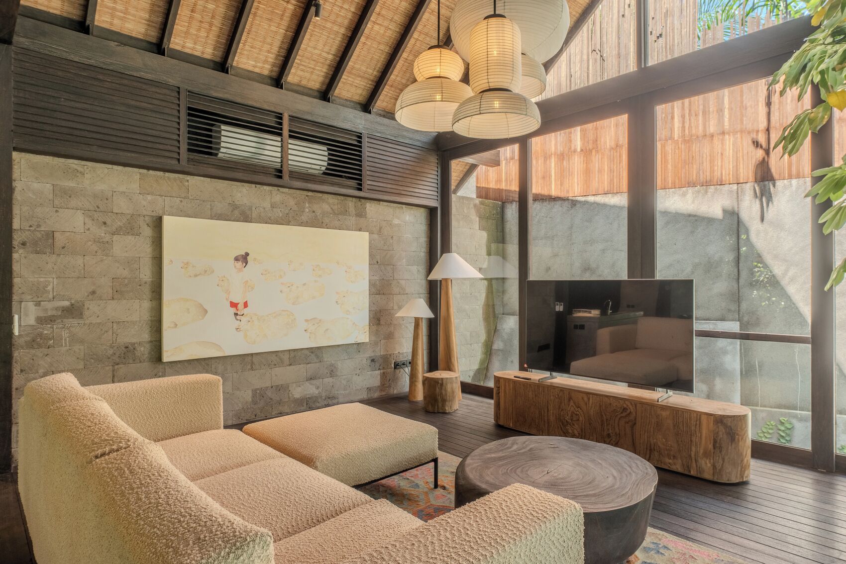 A modern living room with a large TV, comfortable seating, and a large window offering a view of the outdoors.