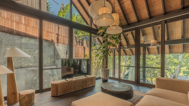 A spacious room with a large TV, wooden furniture, and a large window overlooking greenery. - Rumah Lituhayu (Tabanan)