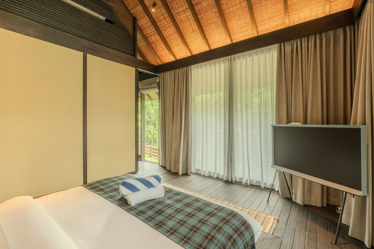 Un dormitorio con cama, televisión y cortinas.