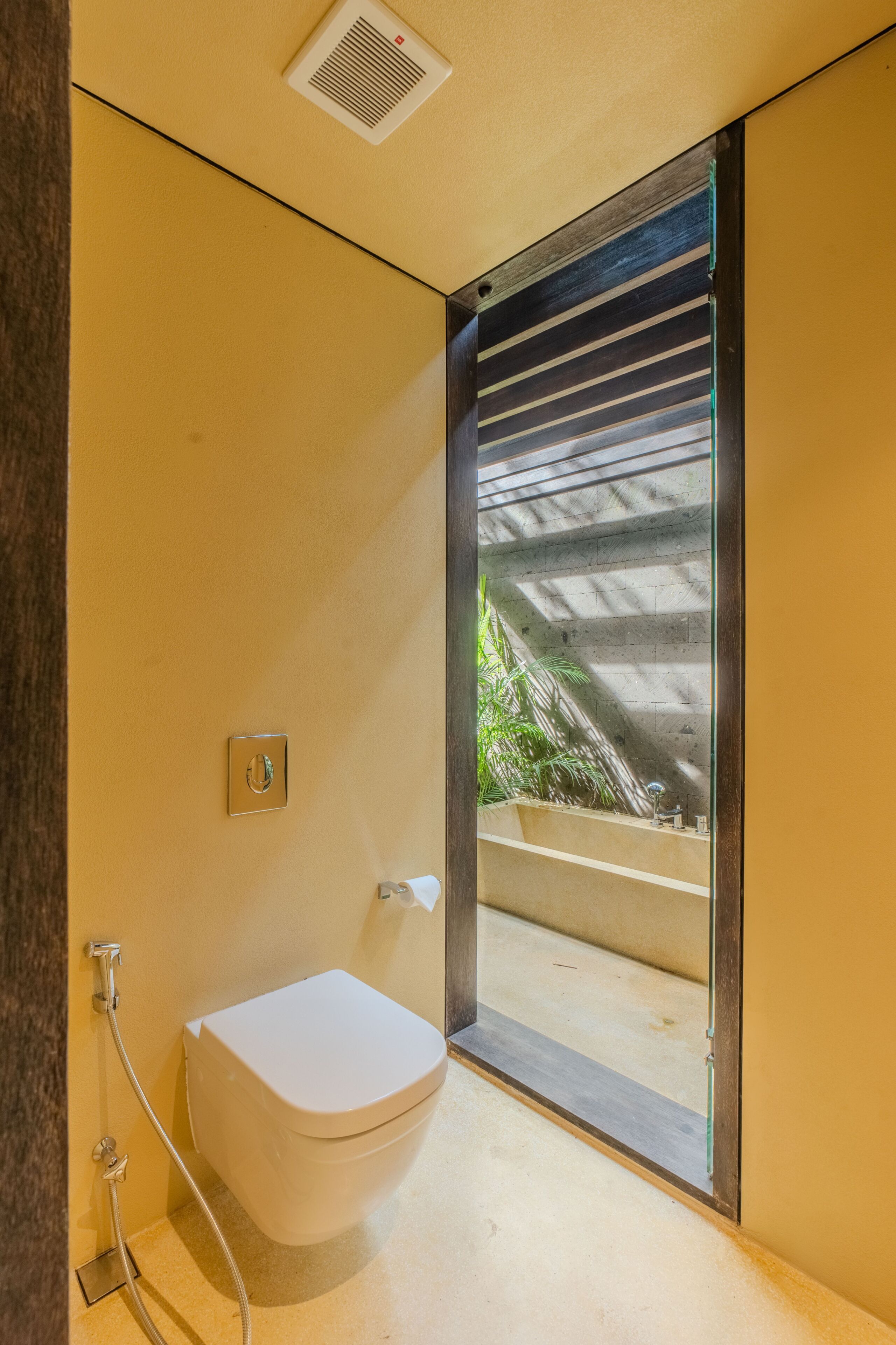 A modern bathroom with a white toilet, a shower, and a glass door leading to an outdoor area.