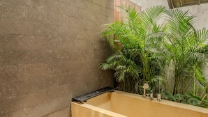 A modern interior with a concrete wall, a wooden ceiling, and a planter with green plants. - Rumah Lituhayu (Tabanan)
