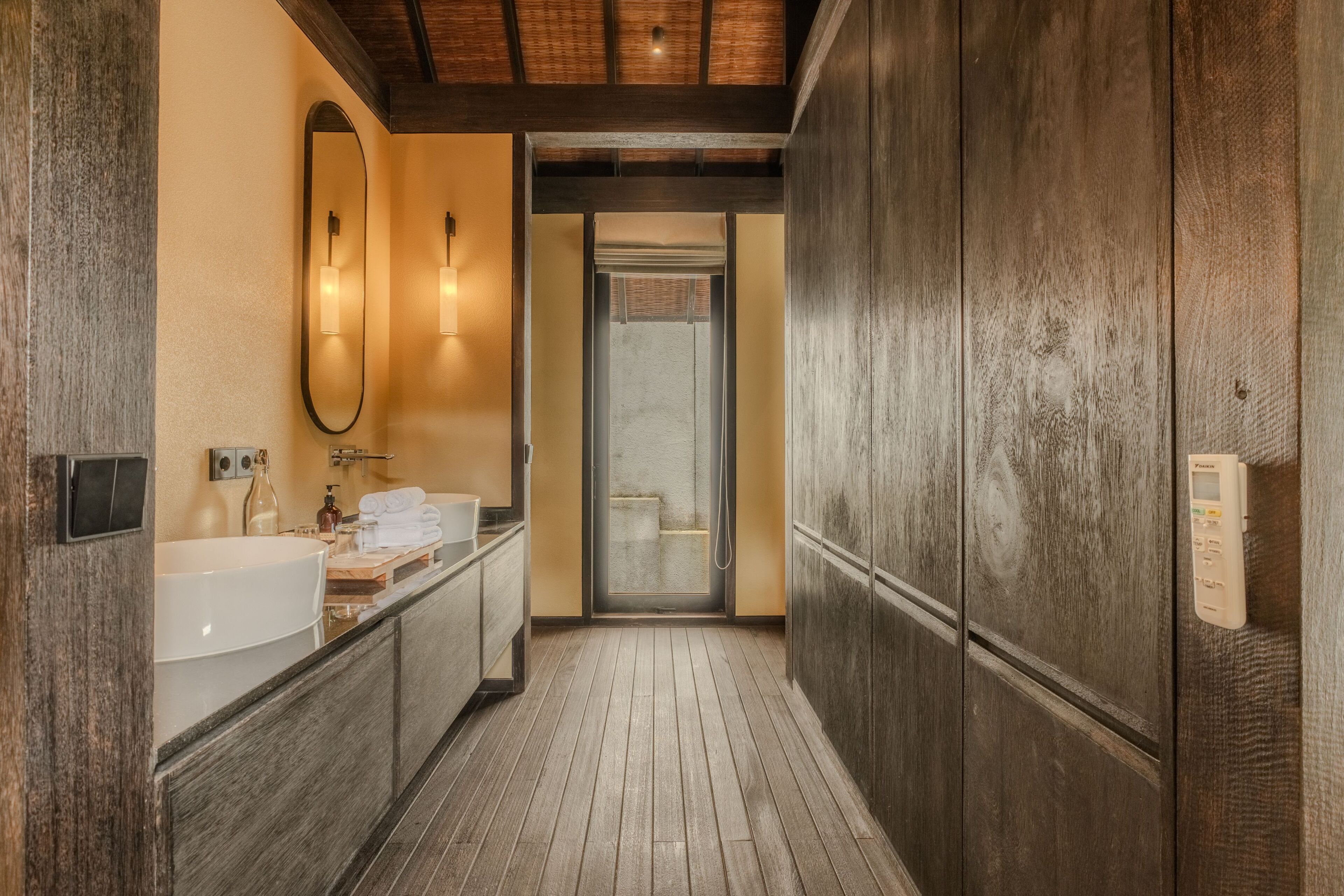 Une salle de bain avec un plancher en bois, un grand miroir, un lavabo et un espace douche.