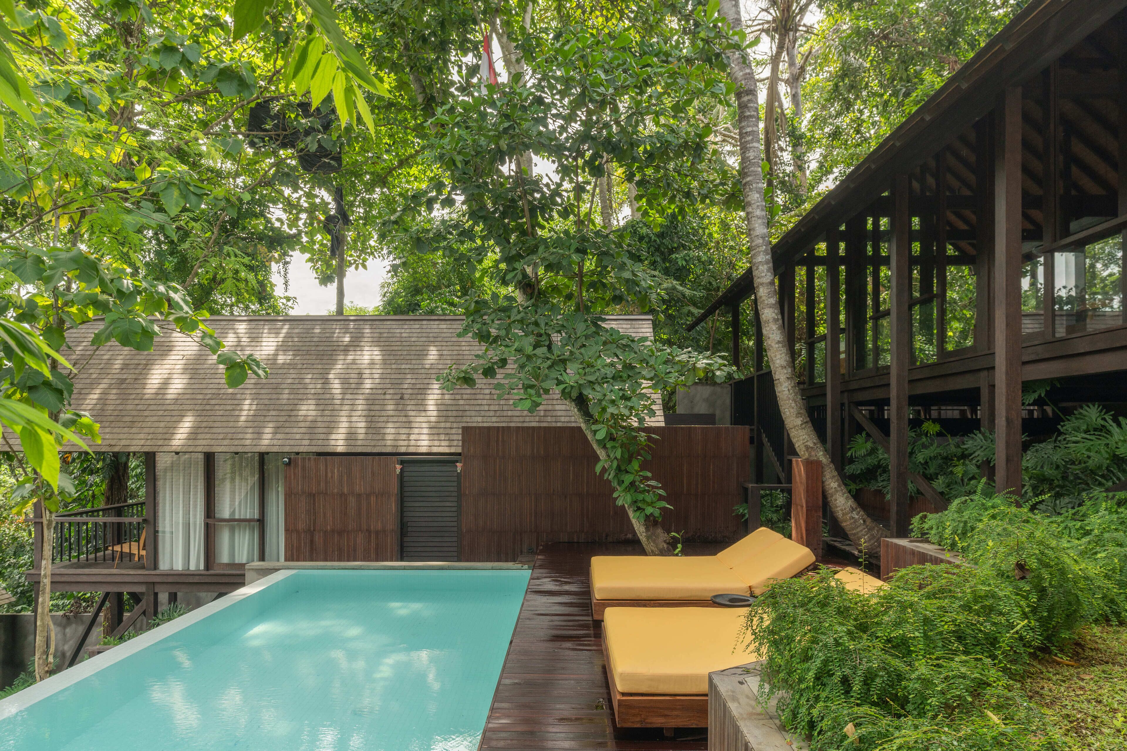 A pool area with wooden deck, lounge chairs, and a covered seating area.