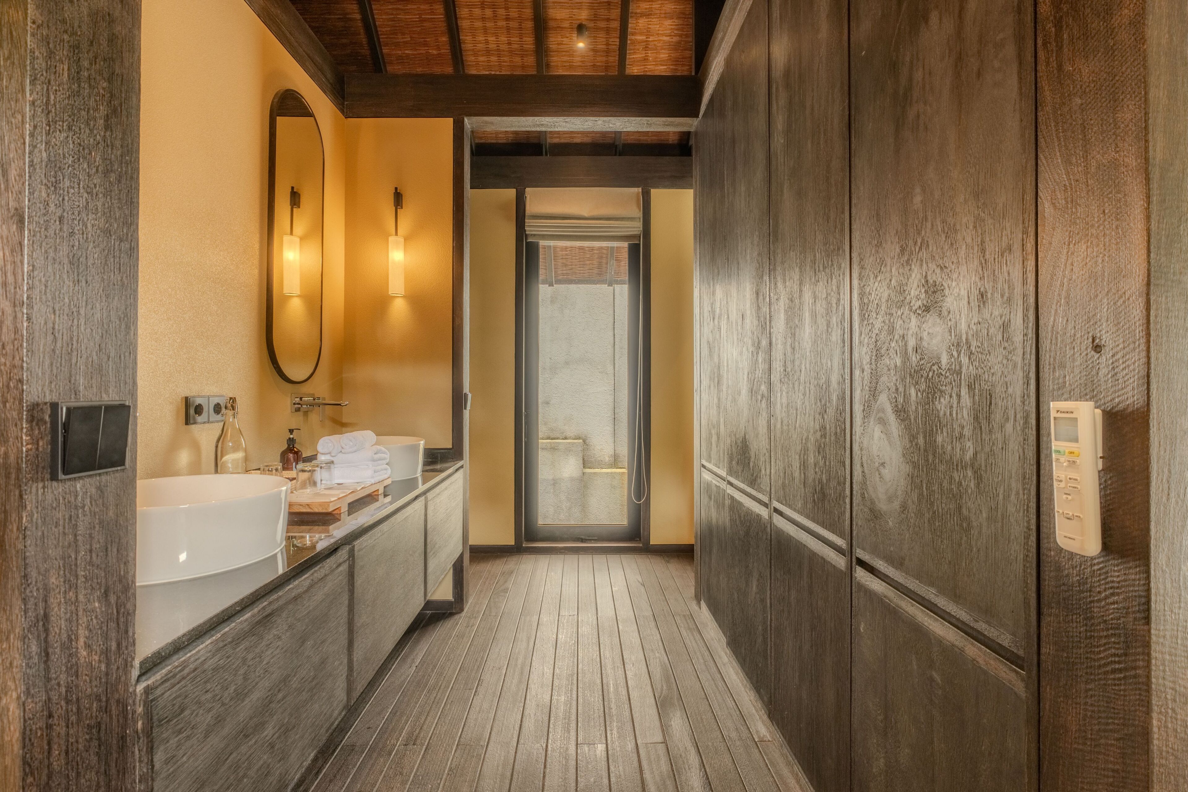 A wooden-floored hallway leading to a bathroom with a sink, mirror, and towel rack.