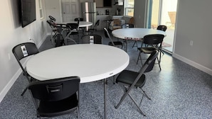 A conference room with a round table, folding chairs, a ceiling fan, and an exit sign. - Cottage 33: Pineapple Place - Waterfront Lodging in Downtown Tavares, FL (Tavares)