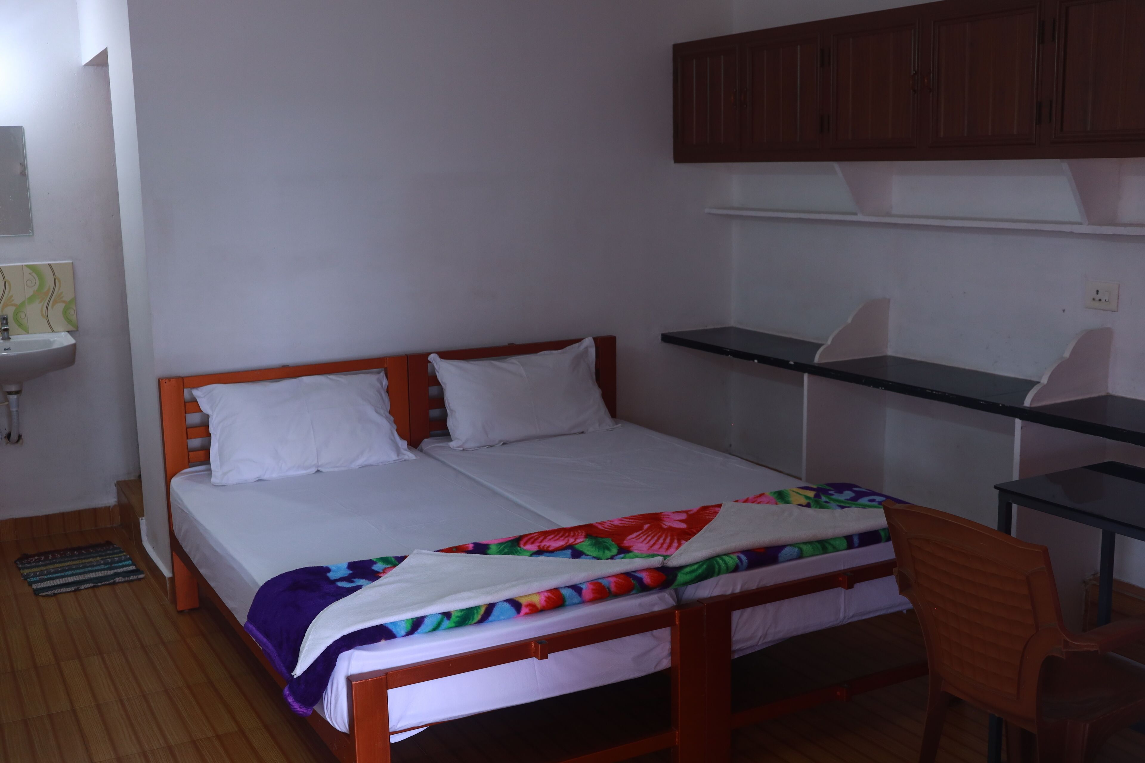 A single bed with a wooden frame, a desk with a chair, and a small sink.
