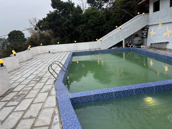 A swimming pool with a tiled edge, a concrete deck, and a staircase leading up to a building with butterfly designs.