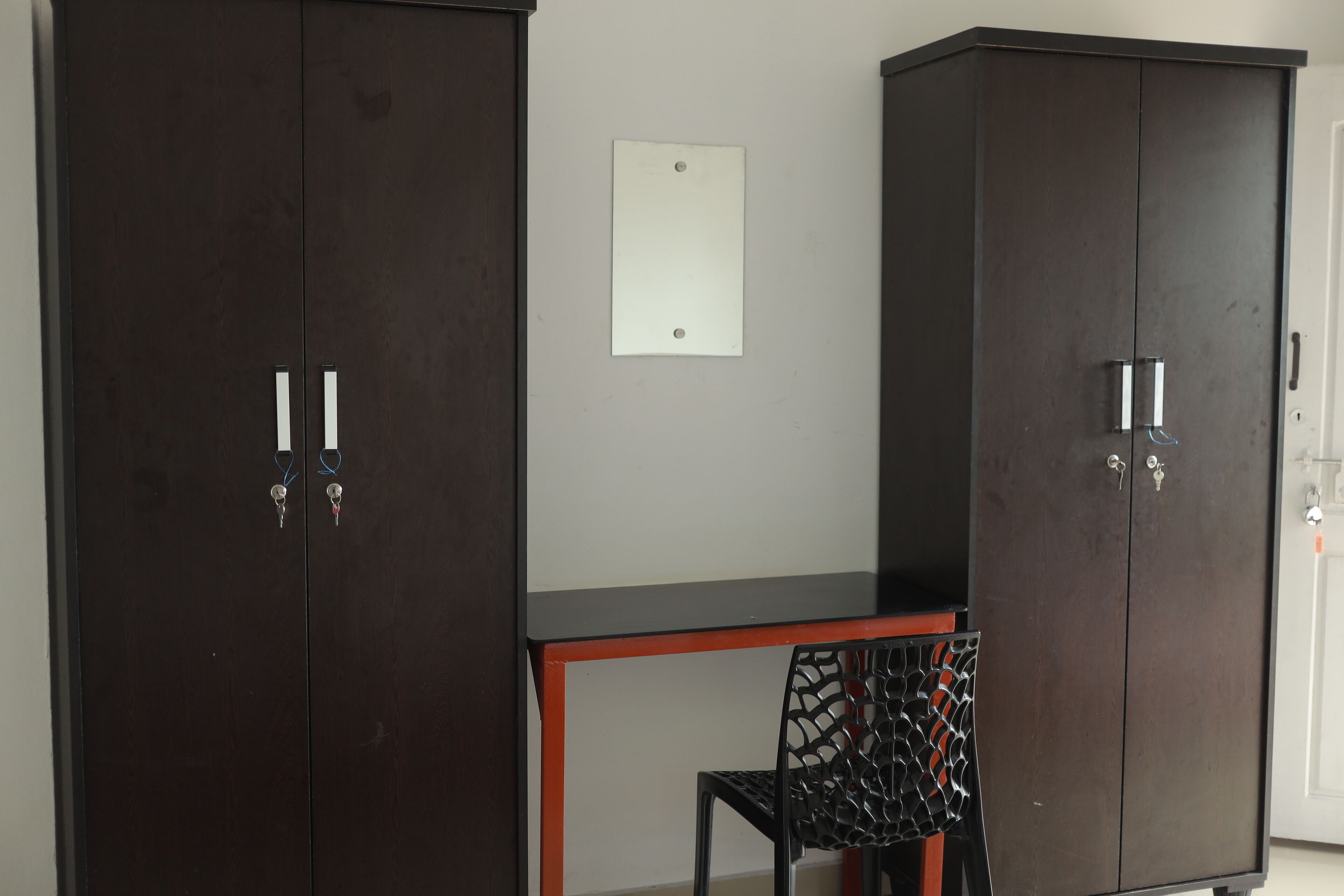 A room with two dark wooden wardrobes, a small table, and a black chair.