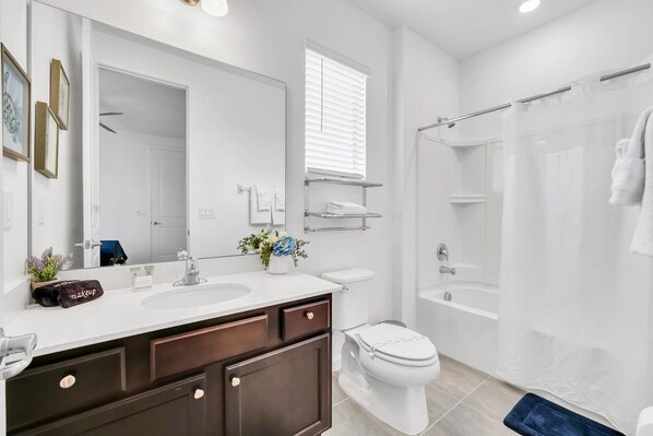 Een moderne badkamer met een wit wastafelmeubel, toilet en douchegordijn. Er is een handdoekhouder.