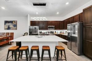 Een moderne keuken met een groot kookeiland, roestvrijstalen apparatuur, houten kastjes en een hanglamp.