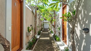A narrow, paved pathway flanked by white walls and wooden doors, leading to a building entrance. - Comoda Seminyak (Seminyak)