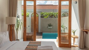 A hotel room with a large bed, a view of a swimming pool, and a balcony with plants. - Comoda Seminyak (Seminyak)