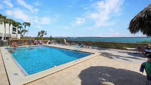 A swimming pool with clear blue water, surrounded by lounge chairs and a wooden deck.