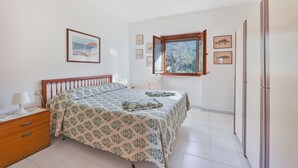 A bedroom with a bed, a nightstand, a dresser, a window with a view, and framed pictures on the wall. - Cala Rossa 40 Pool & Relax (Rio dell'Elba)