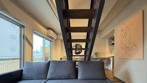 A modern living area with a sofa, a ladder, a dining table, and a kitchen in the background. - 2-Level Group Stay | 10-min to Hiroshima Station (Hiroshima City)