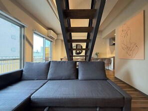 A modern living area with a sofa, a ladder, a dining table, and a kitchen in the background.