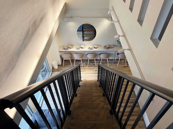 A modern interior with a wooden staircase, a dining area with chairs and a table, and a circular window.