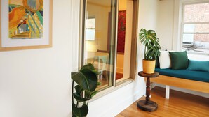 A room with a large window, a framed artwork, a potted plant, a wooden bench, and a teal sofa. - The Maple Flat: high end 2-bedroom apartment in Blairsville (Blairsville)