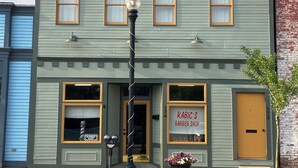 A two-story building with a green facade, a barber shop sign, and a street lamp in front. - The Maple Flat: high end 2-bedroom apartment in Blairsville (Blairsville)