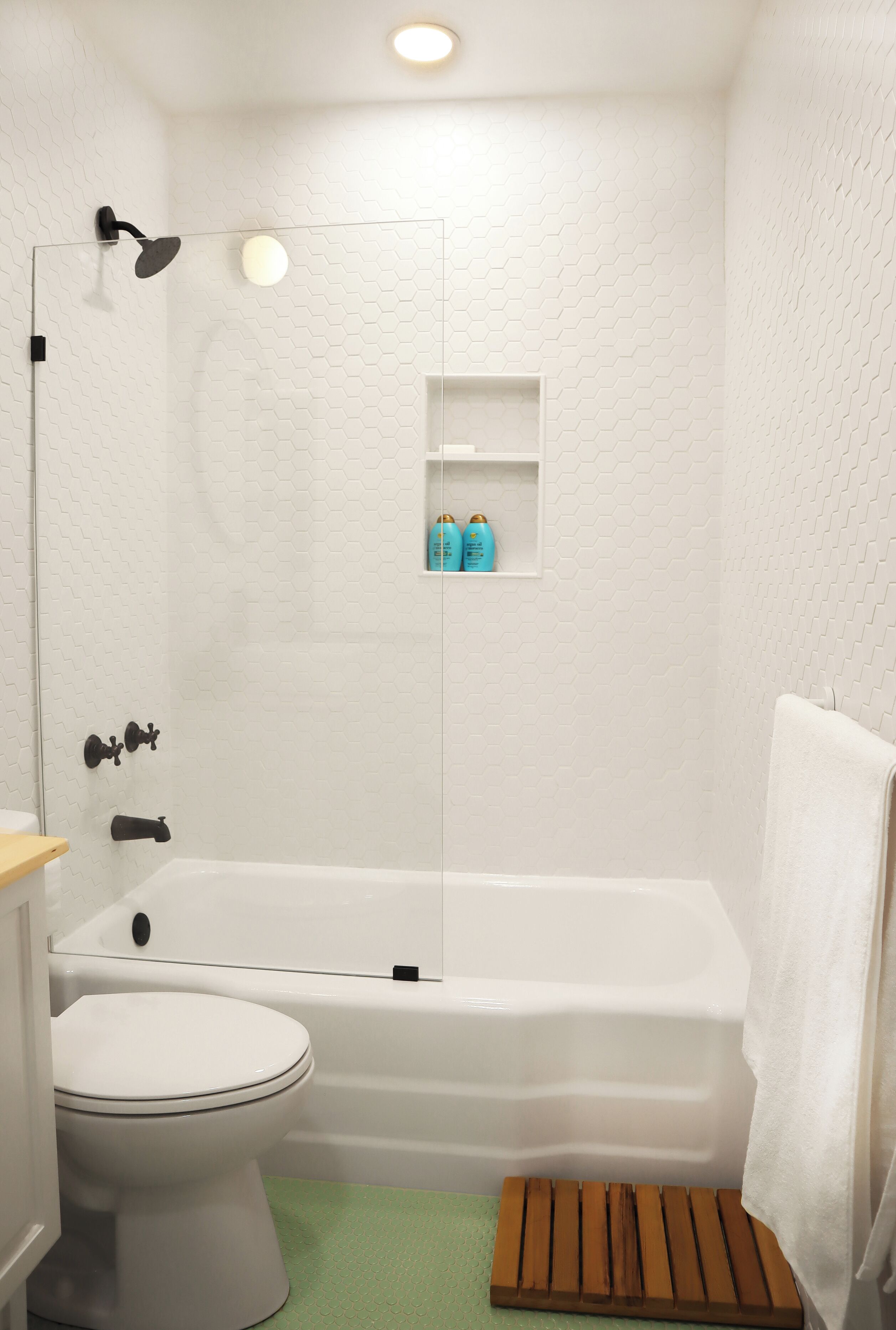 A bathroom with a white bathtub, a toilet, a shower with a glass door, and a shelf with toiletries.