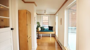 A hallway with wooden flooring, a bench with cushions, a potted plant, and a view of a brick building through a window. - The Maple Flat: high end 2-bedroom apartment in Blairsville (Blairsville)
