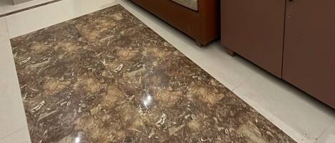 Un interior moderno con una puerta de madera que indica '202', un sofá marrón, un tapete con estampado de mármol y una zona de cocina con mostrador.