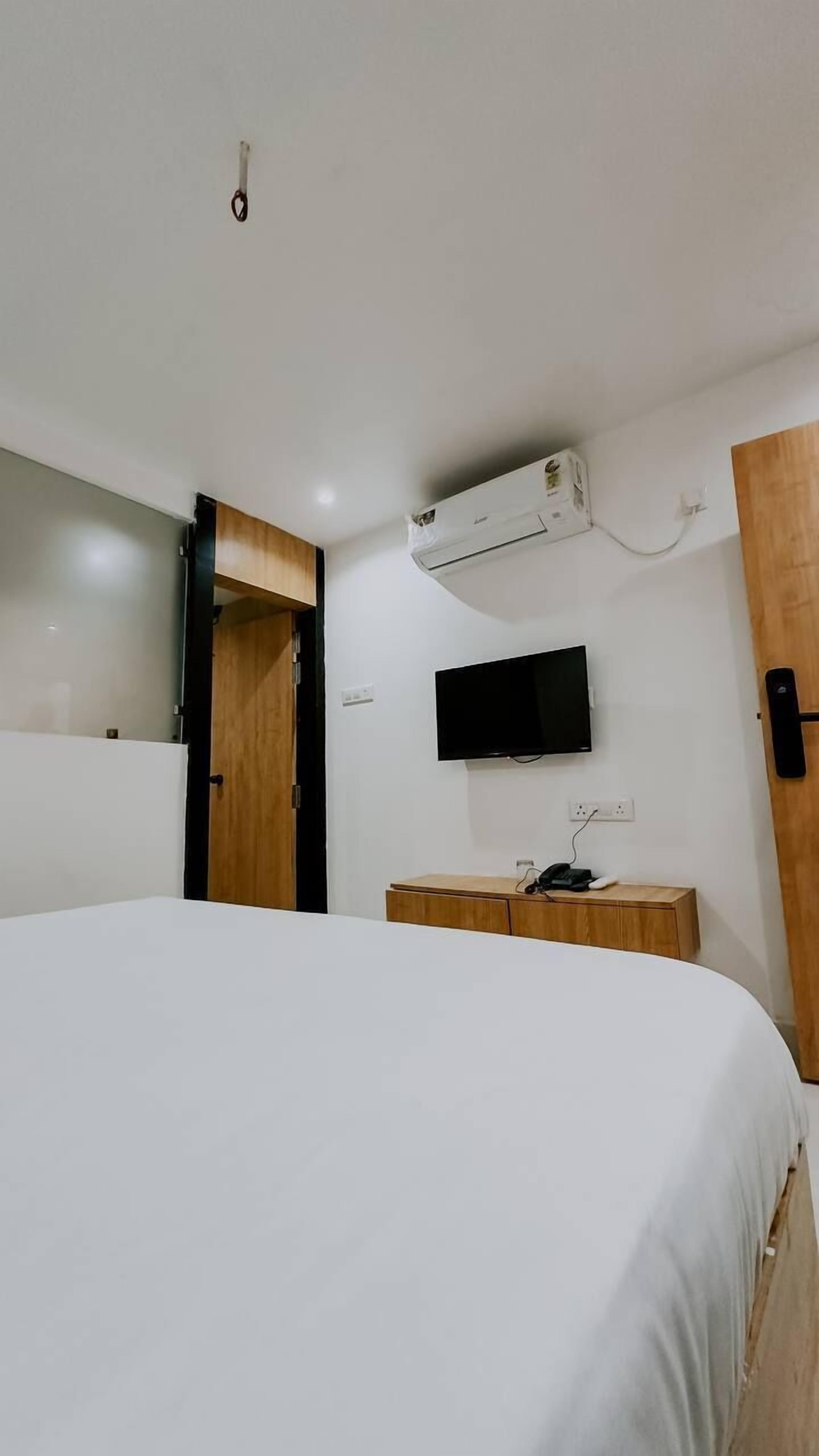 Una habitación de hotel moderna con una cama grande, un televisor de pantalla plana, un equipo de aire acondicionado y un armario de madera.
