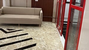 A modern lobby with a marble floor, a beige sofa, wooden panel walls, and red-framed glass doors. - Nirvana Bliss (Prayagraj)