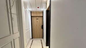 A hallway with a wooden door marked "205", white walls, and a marble-tiled floor with a brown strip. - Nirvana Bliss (Prayagraj)