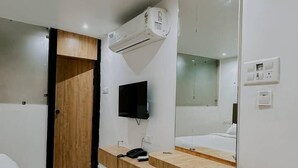 A modern hotel room with a wooden vanity, a large mirror, a flat-screen TV, and a small round table. - Nirvana Bliss (Prayagraj)