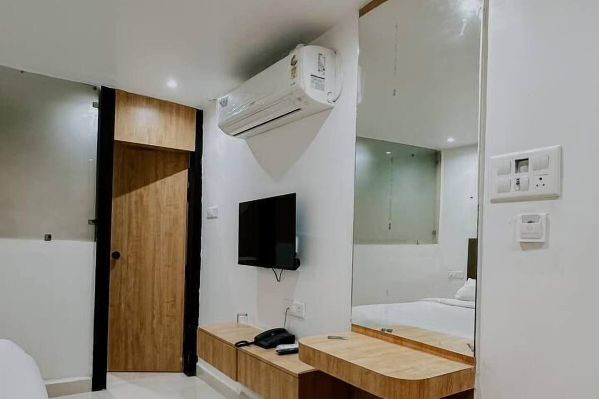 Habitación de hotel moderna con tocador de madera, un espejo grande, televisor de pantalla plana y una pequeña mesa redonda.