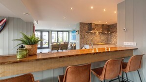 A modern kitchen with a wooden bar, four bar stools, and a large window. - Callantsoog Group Getaway Beach (Callantsoog)