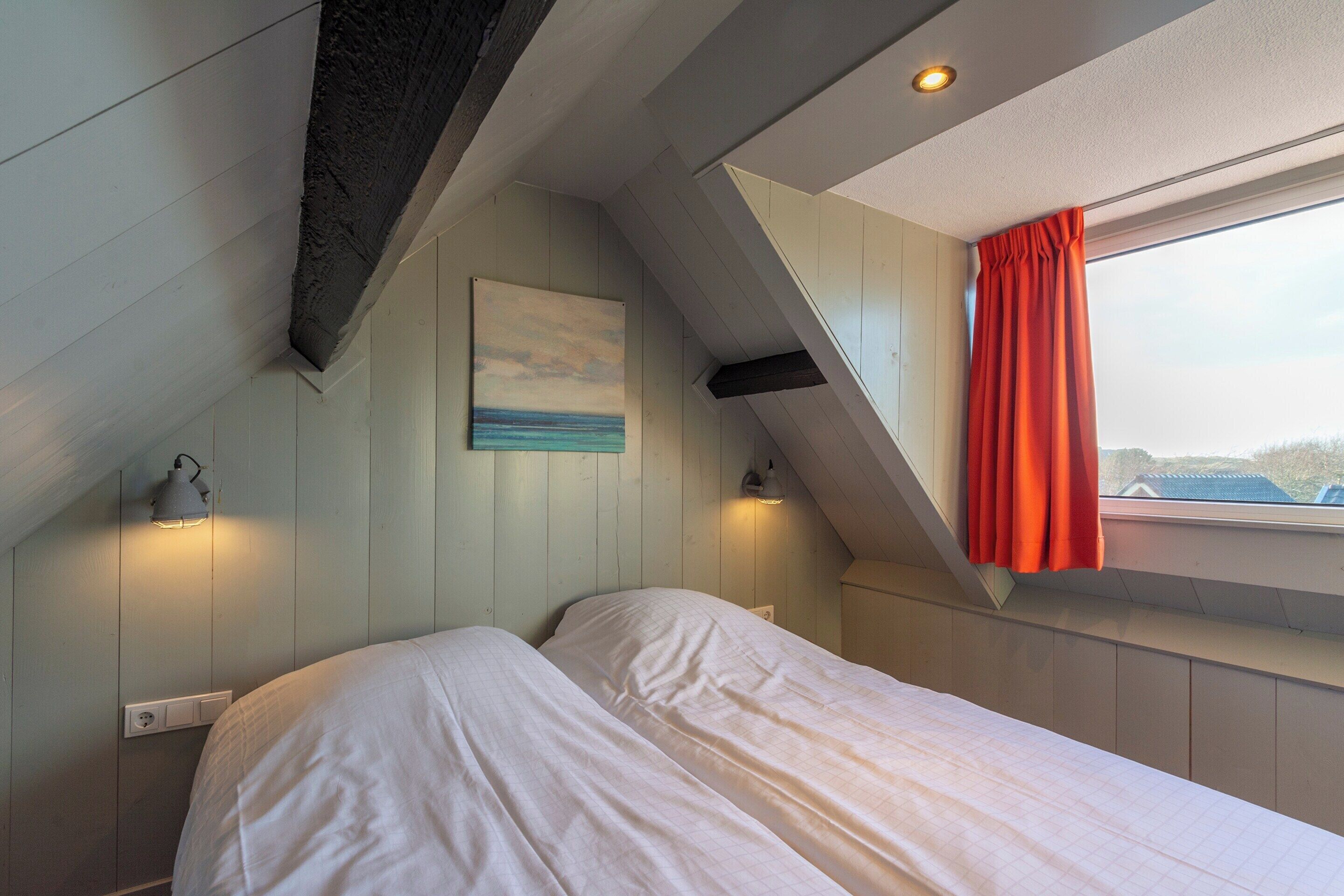 Un dormitorio con techo inclinado, una cama, un cuadro y una ventana con cortinas.