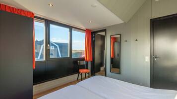 A bedroom with a large bed, a chair, a mirror, and a door.