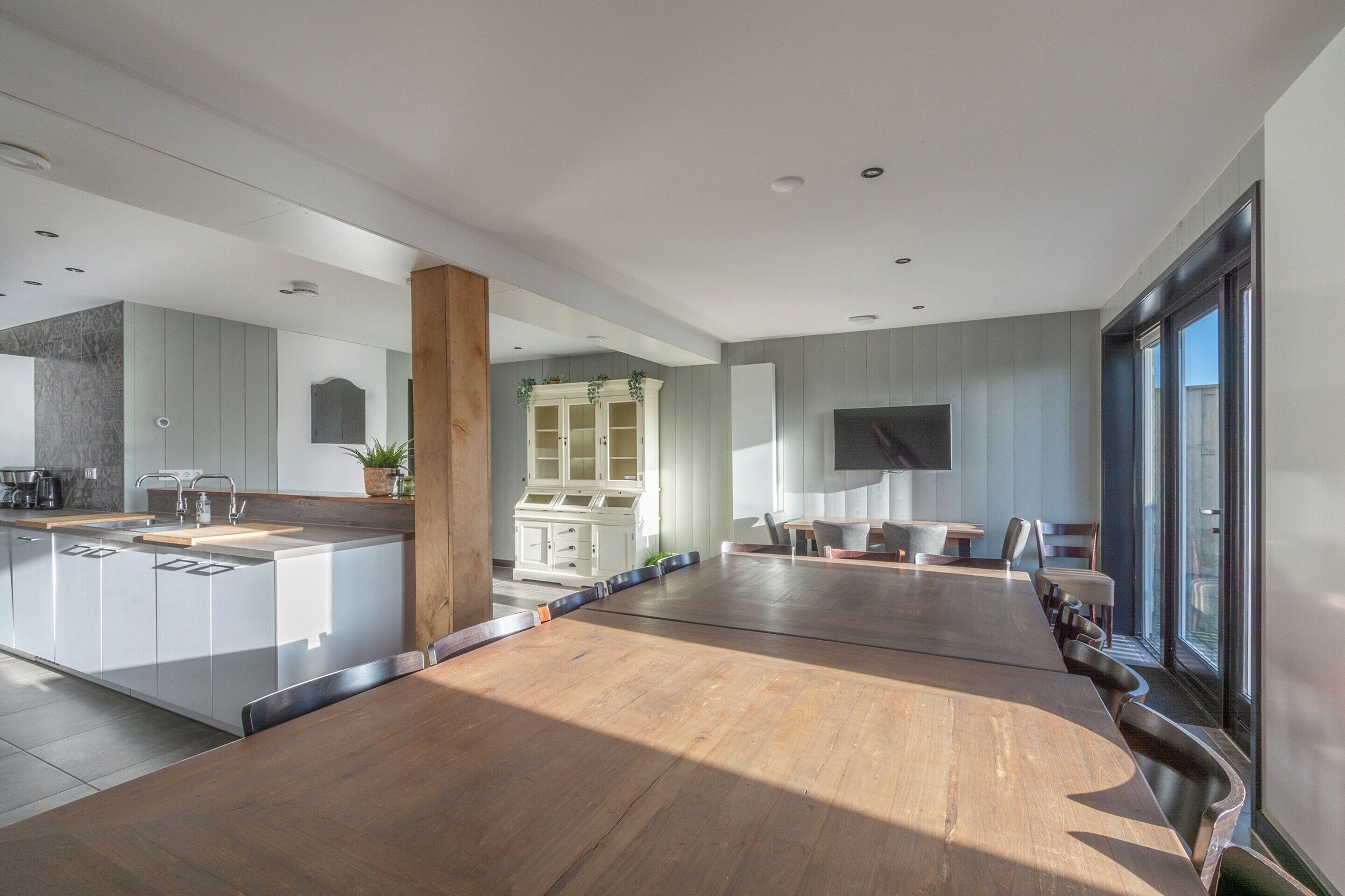 A spacious kitchen with a central island, a dining area with a long table, and a large window providing natural light.