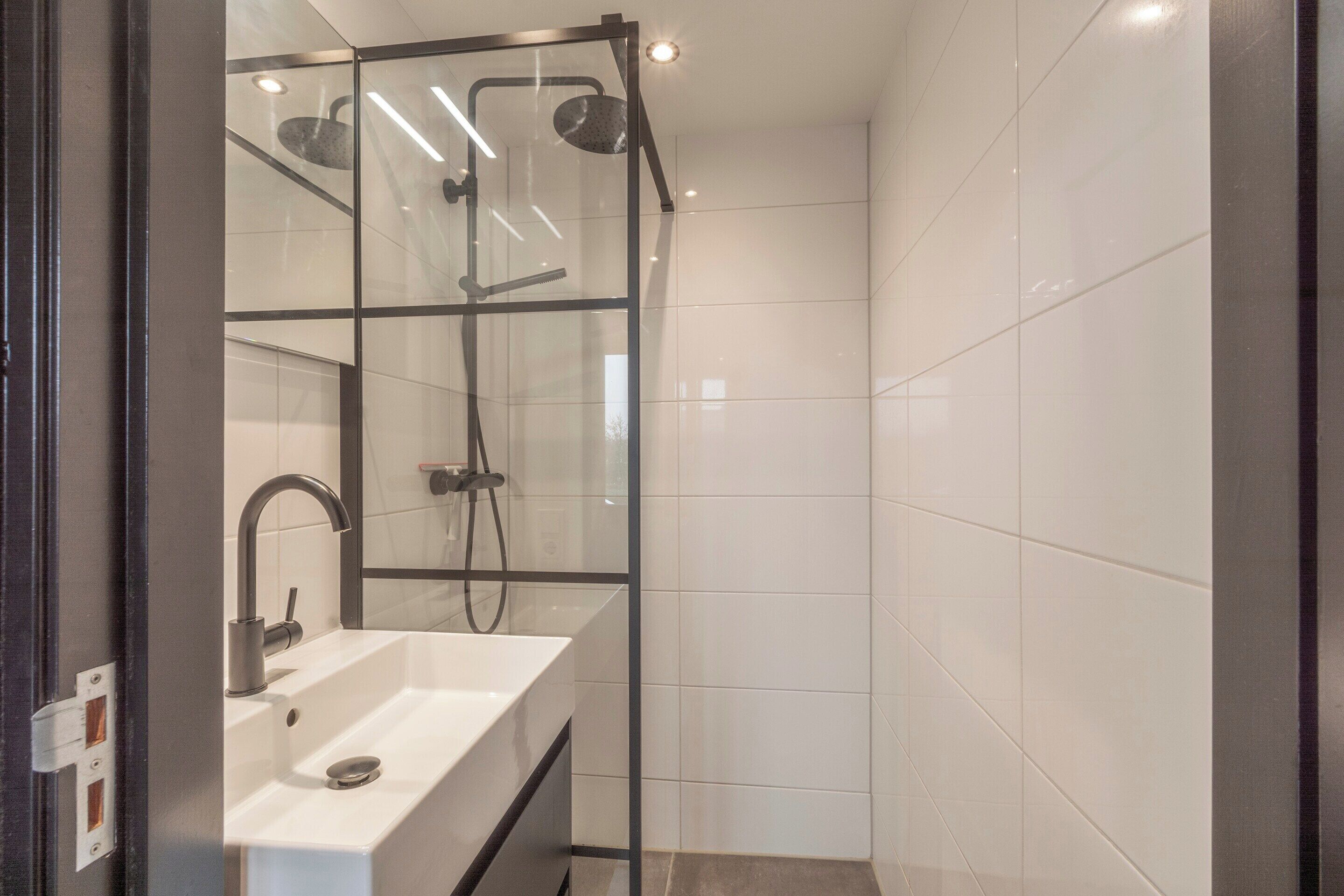 A modern bathroom with a glass-enclosed shower, a white sink, and a mirror.