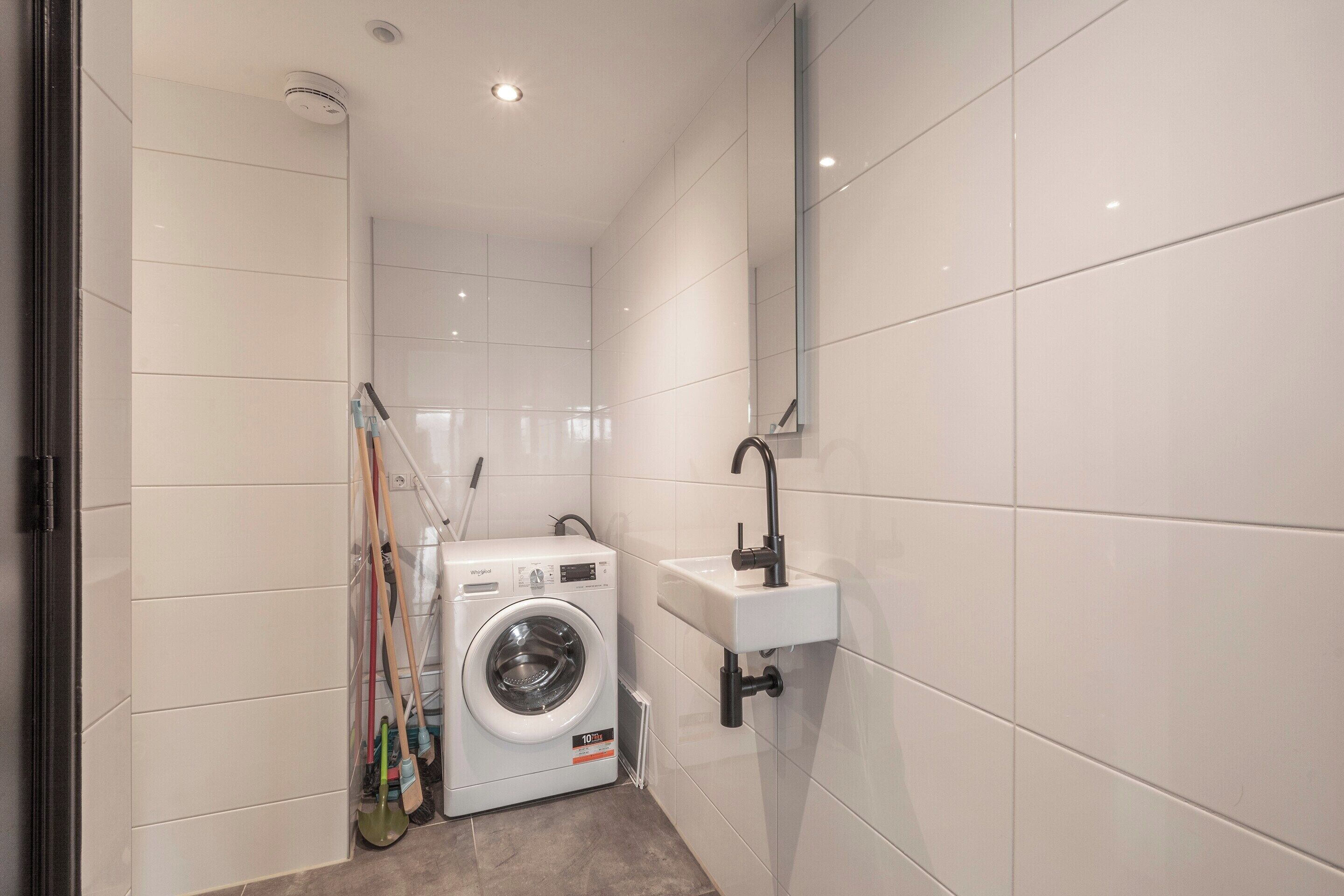 A compact laundry room with a front-loading washing machine, a sink, and a mop rack.