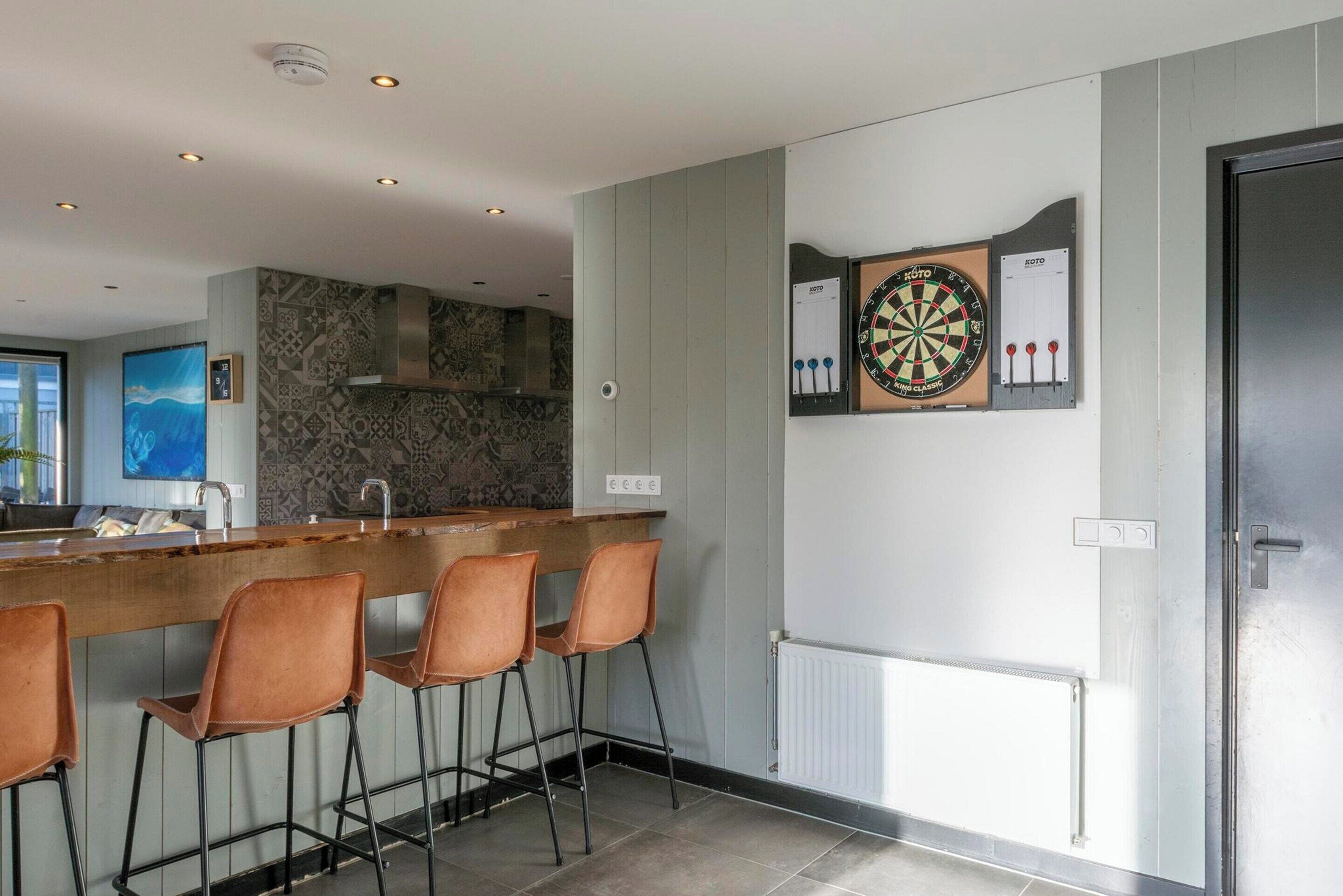 A modern kitchen with a bar area, a dartboard, and a large window.