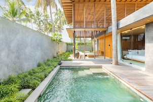 A modern outdoor pool area with a wooden deck, seating, and a view of a building with large windows.
