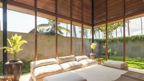 A spacious bedroom with a large bed, a wooden table, and a view of palm trees. - Rumah Amadangi Kedungu (Tabanan)