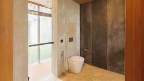 A modern bathroom with a toilet, shower, and a large window. - Rumah Amadangi Kedungu (Tabanan)
