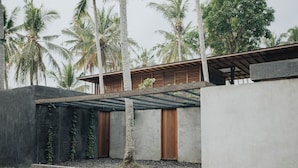A modern building with a concrete facade, wooden doors, and a covered outdoor area. - Rumah Amadangi Kedungu (Tabanan)