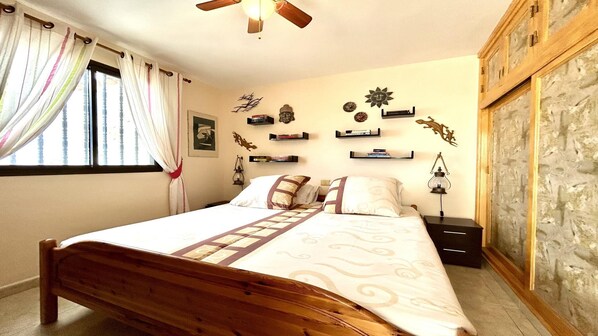 A bedroom with a wooden bed, a ceiling fan, and decorative wall shelves. - stunning and cozy holiday rental with ocean views (Costa Calma (incl. Urbanización Cañada del Río))