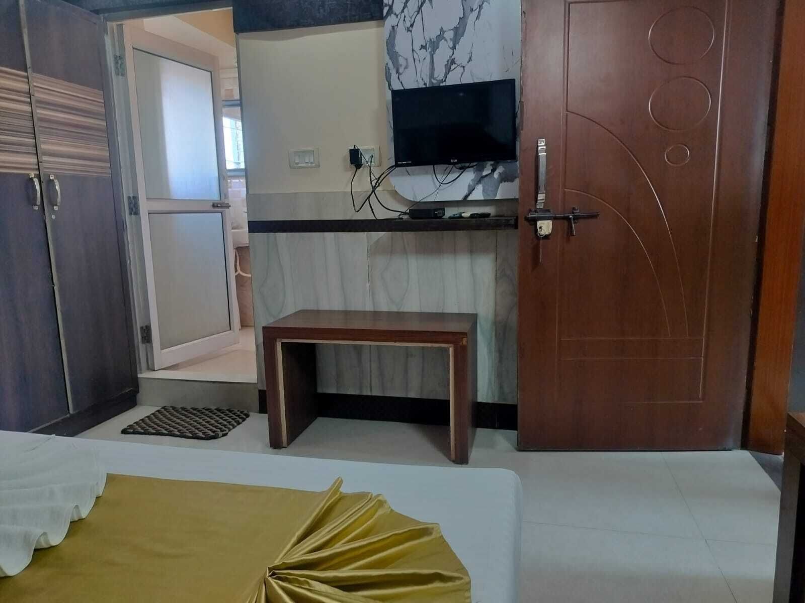Une petite pièce comprenant un lit, une petite table en bois, un téléviseur fixé au mur et une porte dotée d’une poignée ronde.