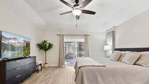 A bedroom with a bed, a TV, a dresser, a ceiling fan, and a window with curtains. - Hialeah Hole in One Golf House (Pinehurst)