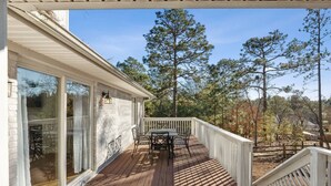 A wooden deck with a table and chairs, a white railing, and a view of trees. - Hialeah Hole in One Golf House (Pinehurst)