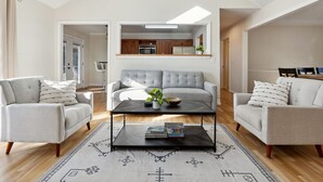 A modern living room with a grey sofa set, a coffee table, and a kitchen area visible through an open doorway. - Hialeah Hole in One Golf House (Pinehurst)
